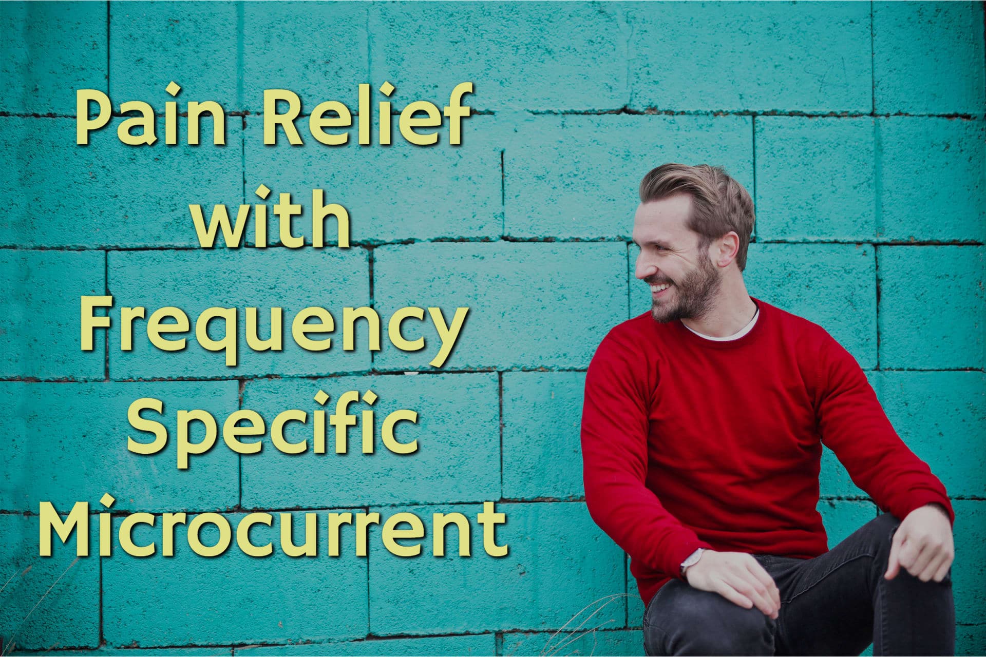Happy man wearing a red long sleeve shirt and black jeans smiling and sitting in front of a blue brick wall after achieving pain relief